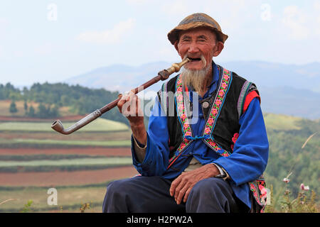 Dongchuan, Cina - 27 Settembre 2016: Un vecchio uomo cinese vestiti con i costumi tradizionali di fumare mentre godendo il panoram Foto Stock