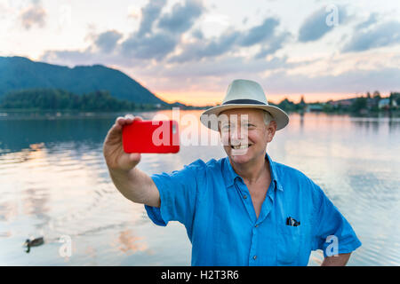 Uomo sorridente, prendendo foto con il telefono cellulare, selfie, Schliersee, Alta Baviera, Baviera, Germania Foto Stock