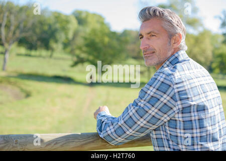 Uomo appoggiato sulla recinzione di legno Foto Stock