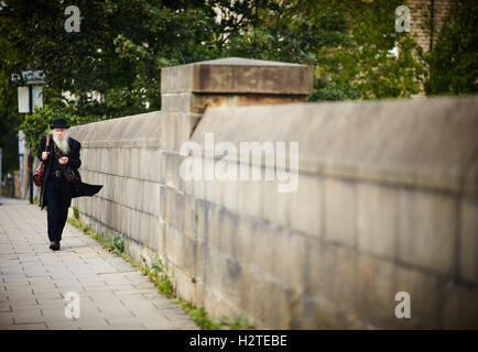 Lancaster caricatura uomo vecchio caricatura con bombetta di camminare su un ponte nel centro della città, nero scuro Abbigliamento e borsa in pelle stile hobo Foto Stock
