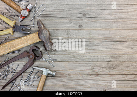 Vecchio strumento Corredo di martelli, pinze, pinze e chiodi su grigio grunge di tavole di legno sfondo Foto Stock
