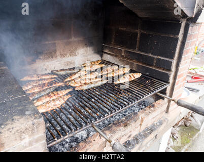 Sardine tostatura su un barbecue Azorian. Un grill pieno di sardine di grigliatura o sgombri cuochi su un barbecue in mattoni su un caldo carbone di legna Foto Stock