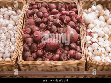 Mazzetto di cipolla rossa, bianca cipolla e aglio nel vassoio di vimini nel supermercato Foto Stock