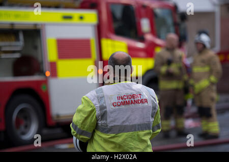 Un incident commander guarda alla scena di un incendio a cui hanno partecipato i vigili del fuoco e un incendio del motore. Foto Stock