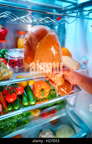 Le mani umane per raggiungere la Turchia gamba cibo durante la notte in frigorifero aperto Foto Stock