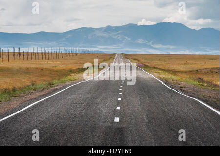 Strada diritta va all orizzonte e montagne Foto Stock