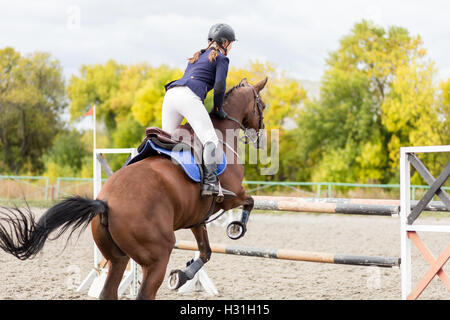 Pilota giovane ragazza sul cavallo saltando un ostacolo sul suo percorso in concorrenza. Sport Equestri show jumping immagine con copia spac Foto Stock