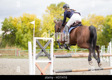 Pilota giovane ragazza sul cavallo saltando un ostacolo sul suo percorso in concorrenza. Sport Equestri sfondo Foto Stock
