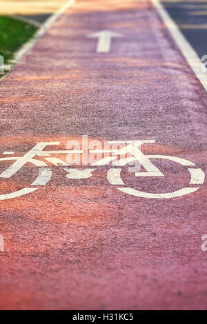 Rosso pista ciclabile sul marciapiede con dipinto di bianco in bicicletta e freccia segni. Spazio di copia Foto Stock