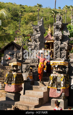 Indonesia, Bali, Amed, privato tempio indù, donna rimozione beata Kunungan offerte attraverso il gateway Foto Stock