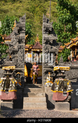 Indonesia, Bali, Amed, privato tempio indù, donna rimozione beata Kunungan offerte attraverso il gateway Foto Stock