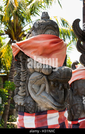 Indonesia, Bali, Lovina, Anturan Village, pietra scolpita testa del serpente con orange saput poleng panno controllati Foto Stock