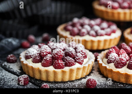 Deliziosa lampone mini crostate (pasticcini) con panna montata su sfondo scuro Foto Stock