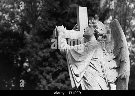 Statua di un angelo che porta una croce lapide lapide presso il cimitero di Highgate East di Londra, Inghilterra. Foto Stock