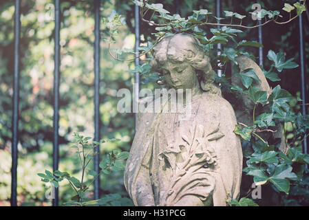 Oggetto contrassegnato per la rimozione definitiva pietra tombale statua di donna angelo con gigli fiori coperti in vigna presso il cimitero di Highgate East di Londra, Inghilterra. Foto Stock