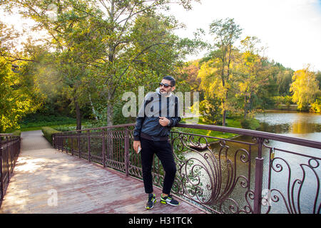 Ritratto di giovane barbuto bello fashion traveler nel parco con uno stile informale e moda pettinatura e zaino e sma Foto Stock