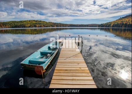 Canotto accanto a un dock sul con le nuvole e alberi riflettendo sull'acqua durante l'autunno nel Maine. Foto Stock