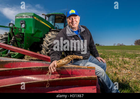 Contadino con pinza a crimpare a rullo su un trattore John Deere Foto Stock