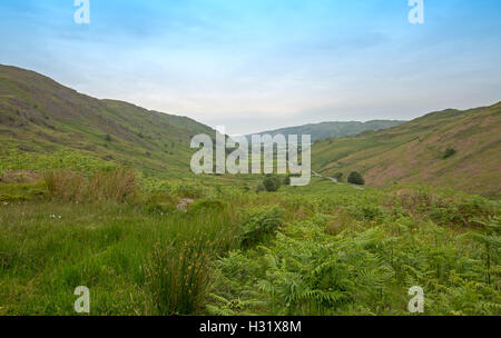 Paesaggio di Emerald brulla colline erbose hemming profonda valle con stretti tornanti per Hard Knott passano in distanza, Lake District, Cumbria Inghilterra England Foto Stock