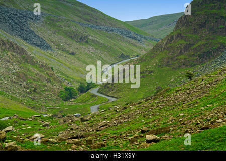 Strada stretta con auto serpeggiando attraverso la profonda valle tra sassoso brulla colline smeraldo a Honister Pass nel Lake District Cumbria, Inghilterra Foto Stock