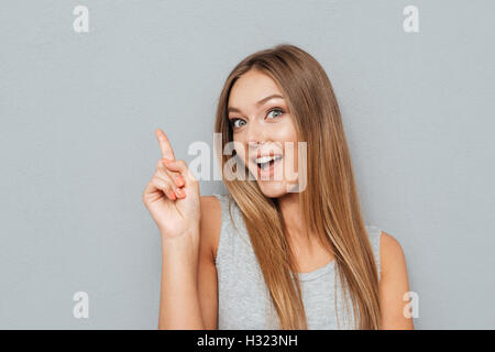 Giovane donna felice poiting dito fino a copyspace isolato su sfondo grigio Foto Stock