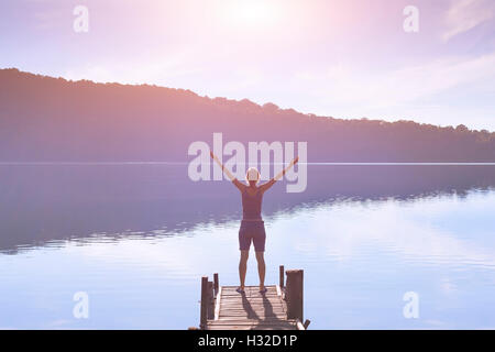 Donna felice alzando le mani in segno di successo e rivolta verso l'alba luce Foto Stock