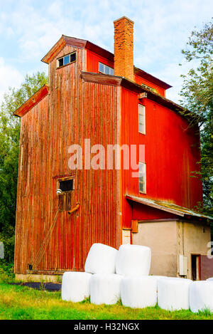 In legno rosso edificio adibito allo stoccaggio o vintage casa colonica con il bianco le balle per insilamento di fronte. Foto Stock