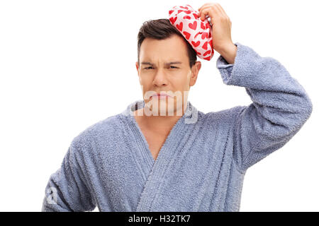 Giovane uomo in accappatoio con un mal di testa e di trattenimento di un pacchetto di ghiaccio isolato su sfondo bianco Foto Stock