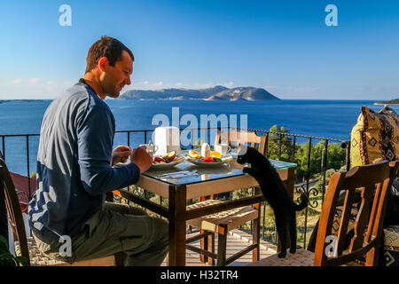 Uomo con colazione in un hotel con una vista spettacolare e cat guardando nel suo piatto Foto Stock