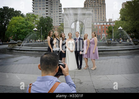 Un asiatico fotografo prende una foto di gruppo di una festa di nozze intorno alla fontana di Washington Square Park in Greenwich Village. Foto Stock