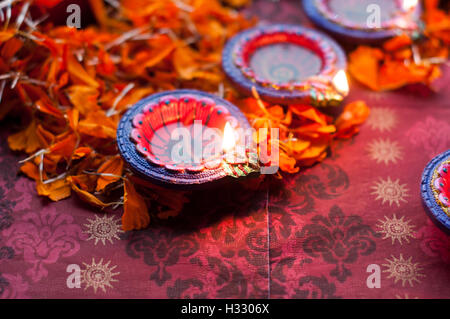 Diya lampade accese durante il Diwali celebrazione con fiori e dolci in background Foto Stock