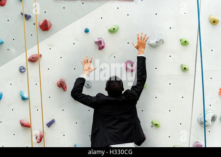 Business man si arrampica su un muro di pratica di arrampicata Foto Stock