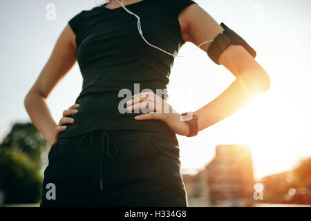 Ritagliato colpo di montare la giovane donna in piedi con le mani sui fianchi. Urban runner all'aperto nella mattina di sole. Foto Stock