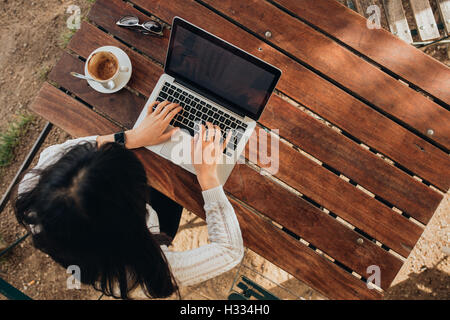 Vista aerea del giovane femmina lavorando sul suo computer portatile presso una caffetteria. Vista Top Shot della donna seduta al tavolo con una tazza di caffè b Foto Stock