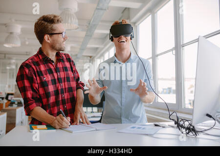 Colpo di due giovani uomini test di realtà virtuale bicchieri in ufficio. Imprenditore indossando occhiali VR e collega la scrittura di note. Foto Stock