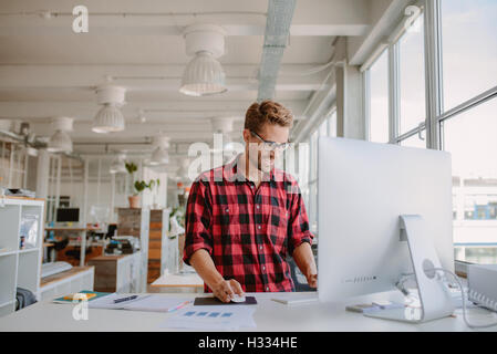 Colpo di felice giovane uomo che lavora sul computer desktop in un moderno ambiente di lavoro. Il giovane imprenditore lavora all'avvio. Foto Stock