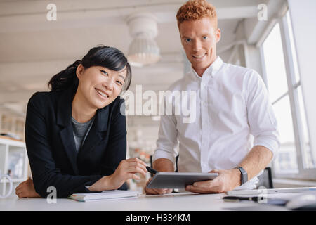 Ritratto di giovane di successo business partner in piedi su un tavolo o in ufficio con tavoletta digitale a portata di mano. Gli imprenditori utilizzando d Foto Stock