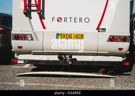 Una tavola da surf di cui al di sotto di una Dethleffs Fortero camper in Sennen Cove car park, Cornwall Foto Stock