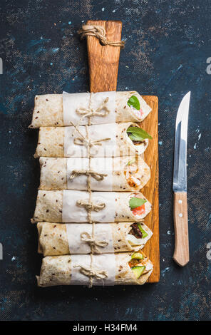 Tortilla avvolge con diversi riempimenti su grigio scuro dello sfondo in calcestruzzo Foto Stock