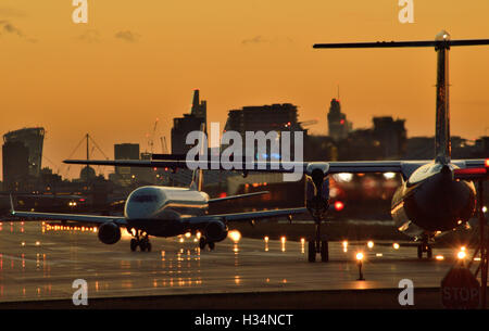 BA Cityflyer Express Limited back-vie mentre FlyBe Dash 8 attende di decollare dal London City Airport come il sole tramonta Foto Stock