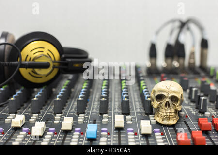 Cranio umano in appoggio su di un mixer audio. Sullo sfondo delle console mixer e cuffie. Foto Stock