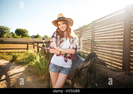 Gioiosa redhead giovani cowgirl preparazione di sella per equitazione al ranch Foto Stock