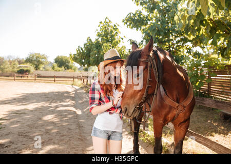 Carino giovane donna cowgirl avendo cura e abbracciando il suo cavallo al ranch Foto Stock