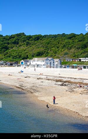 I villeggianti rilassante sulla spiaggia con capanne ed edifici del comune per la parte posteriore, Lyme Regis, Dorset, England, Regno Unito, Europa. Foto Stock