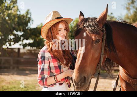 Carino bella giovane donna cowgirl prendendo cura di lei di cavalli sul ranch Foto Stock