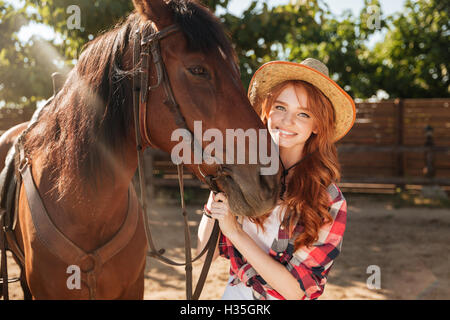 Allegro bella giovane donna cowgirl in hat con il suo cavallo in villaggio Foto Stock