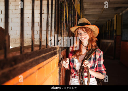 Ritratto di felice bella giovane donna cowgirl in piedi in stabile Foto Stock