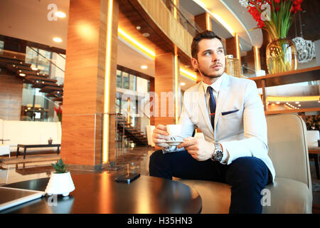 Ritratto di bello uomo di successo bere il caffè seduti in una caffetteria, business man aventi la colazione nella lobby dell'hotel. Foto Stock