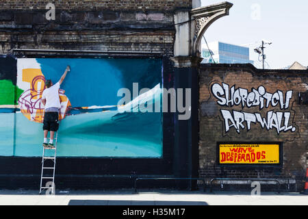 Un artista di strada una pittura murale a parete in Shoreditch, Londra, Regno Unito. Foto Stock