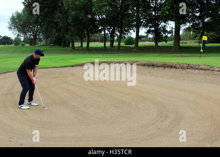 Maschio adulto golfista prendendo un bunker shot con la sfera nella sabbia Foto Stock